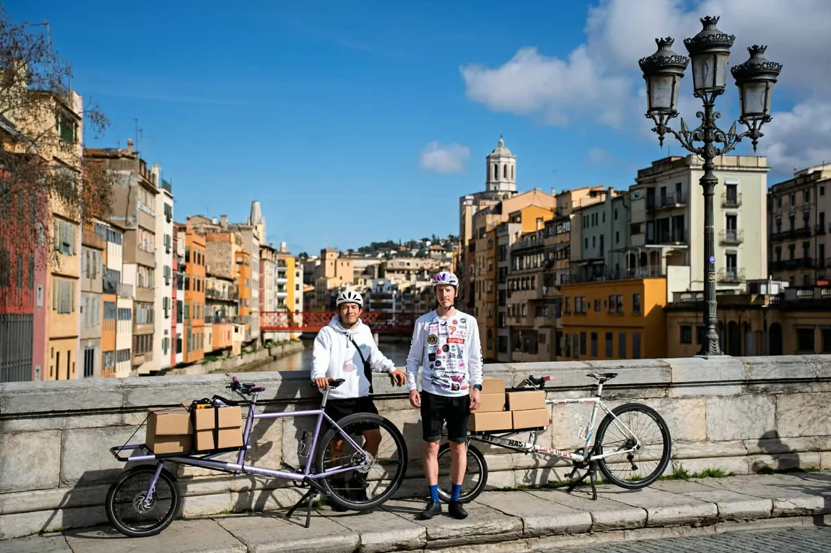 Two Earlybird riders standing by their loaded cargo bikes on a stone bridge