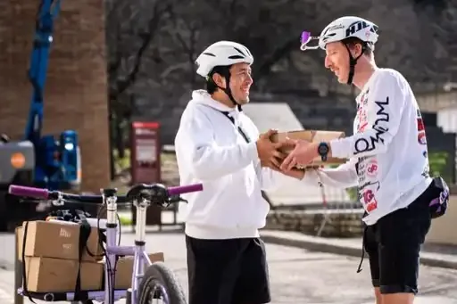 Two riders handing over a cardboard box next to a cargo bike