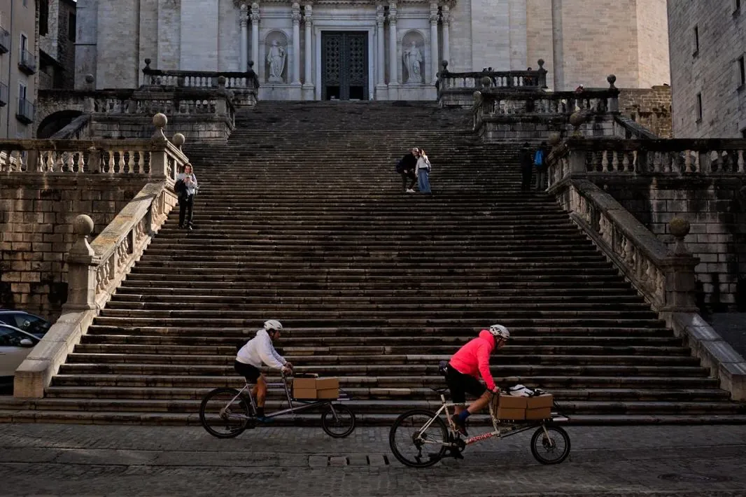 Two Earlybird riders with boxes on their cargo bikes passing a wide stone staircase